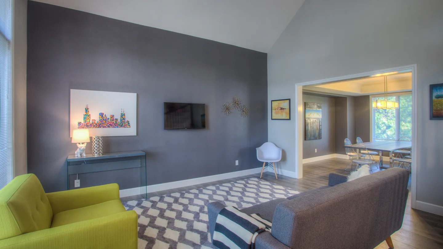 A living room with a sofa, armchairs, a wall-mounted television, framed art and a patterned rug
